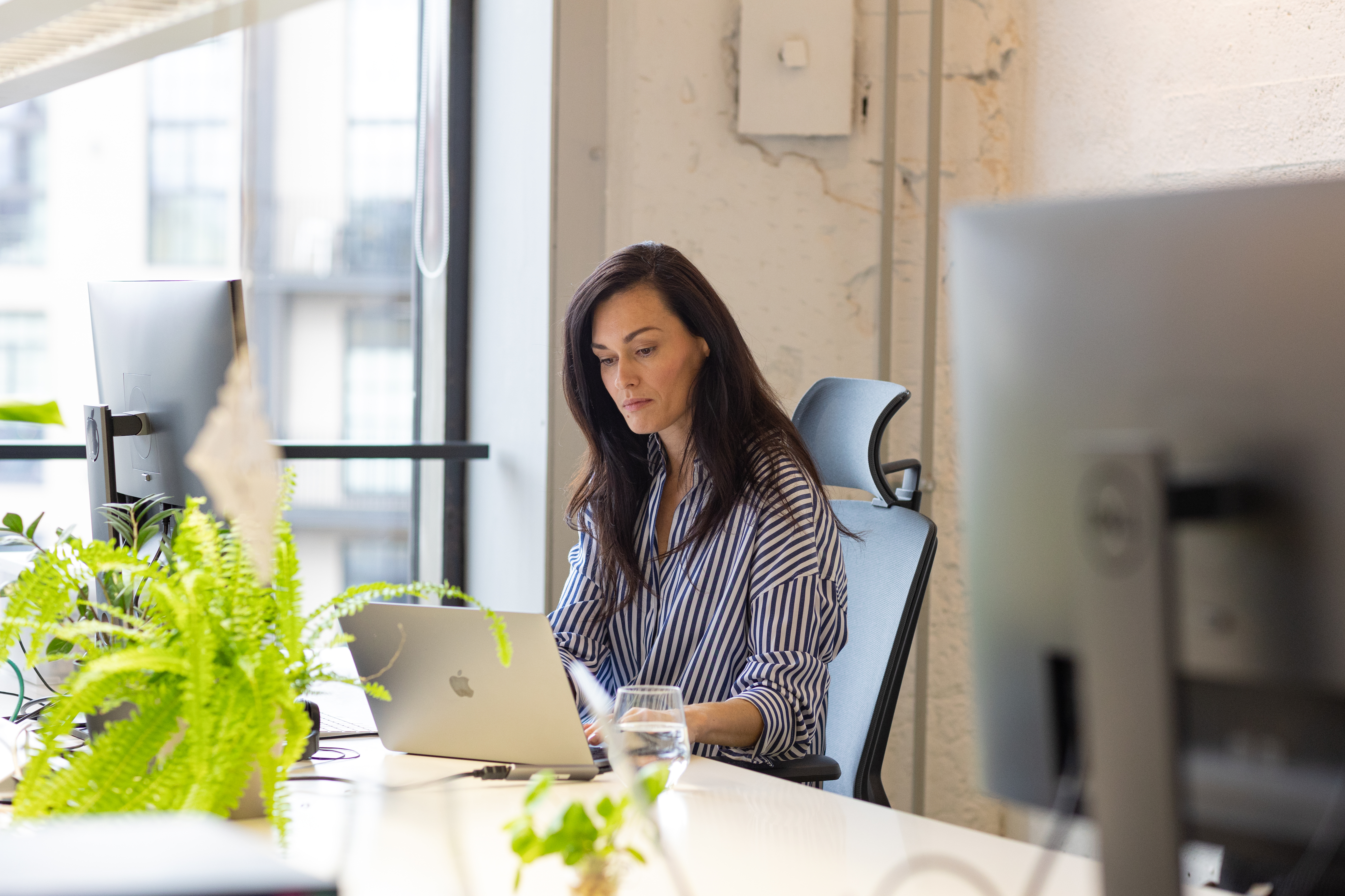 Naine istub kontoris laua taga ja töötab sülearvutiga.