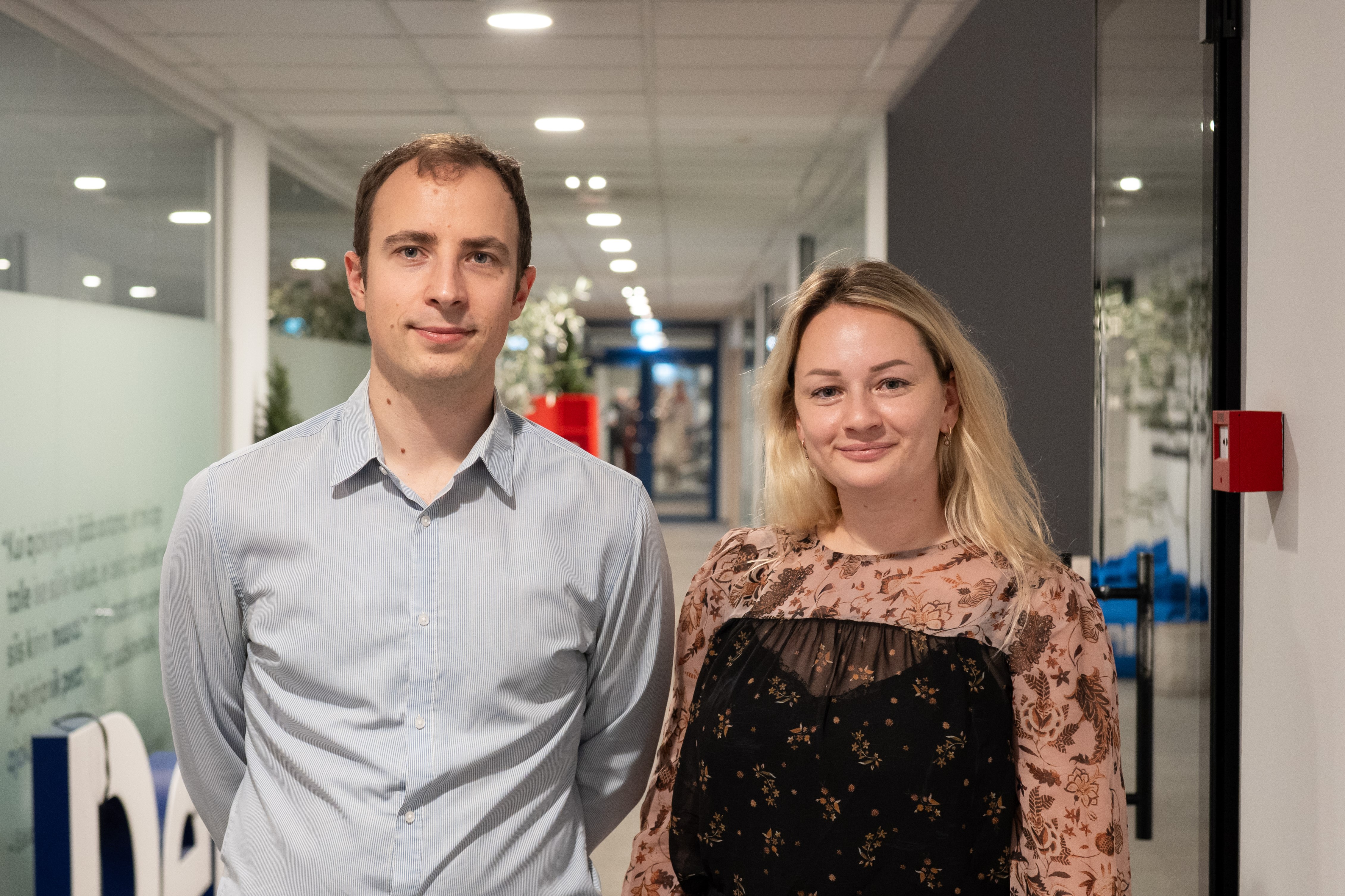 Мужчина и женщина стоят рядом в офисном коридоре.