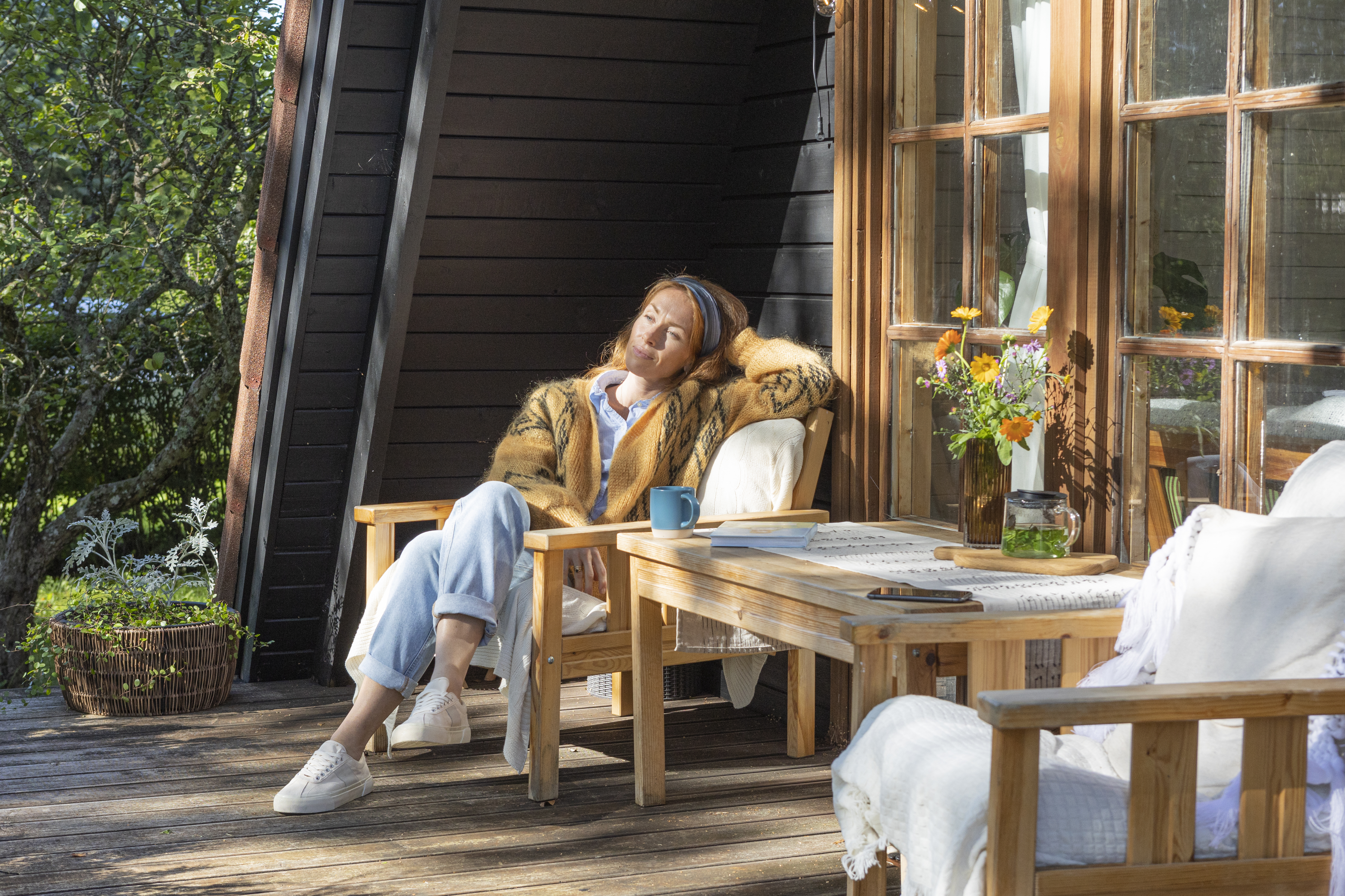 Женщина отдыхает на солнечной террасе, сидя в деревянном кресле.
