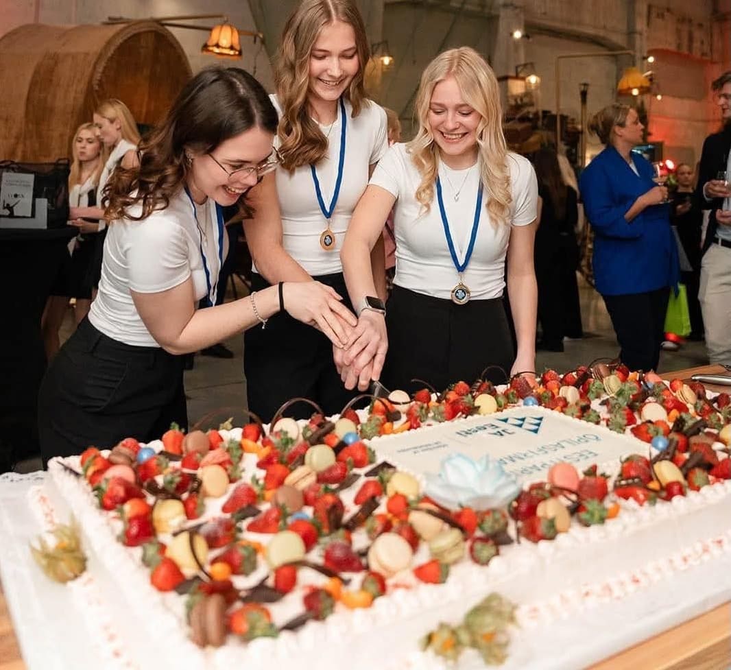 Three young women smile as they cut a large cake.