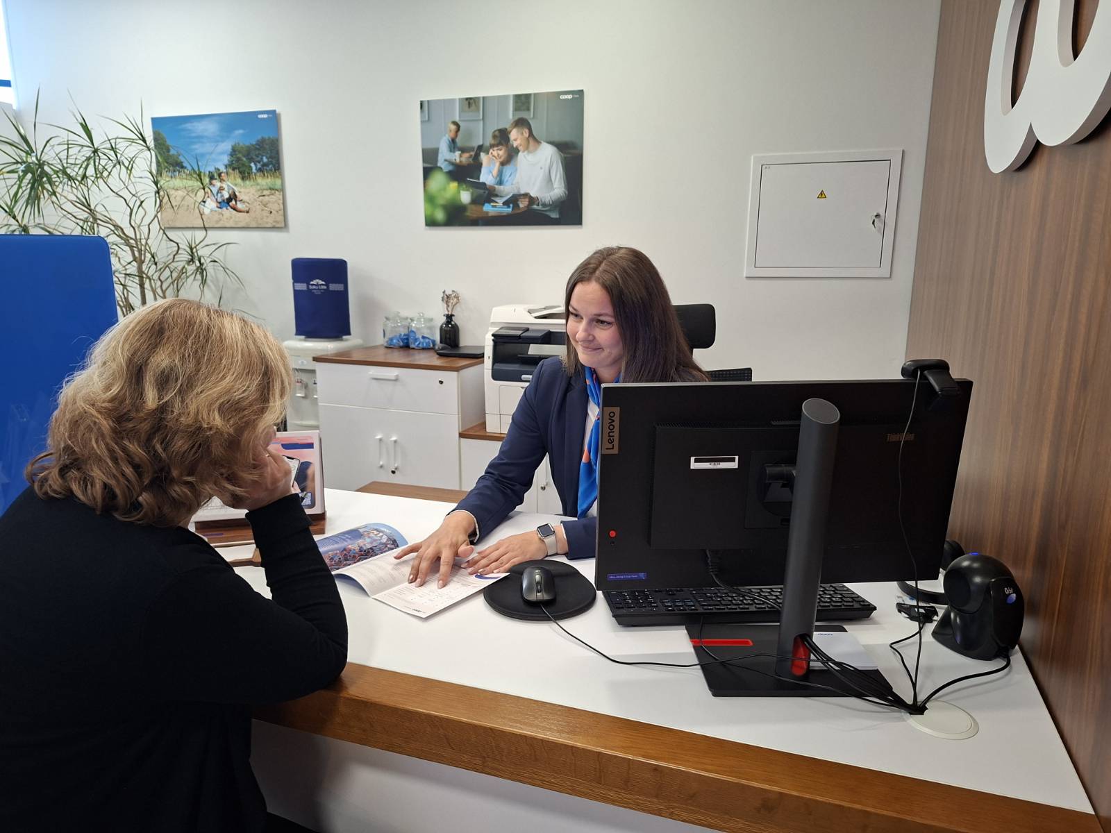 Klienditeenindaja tutvustab pangakontoris laua taga istuvale kliendile infovoldikut.