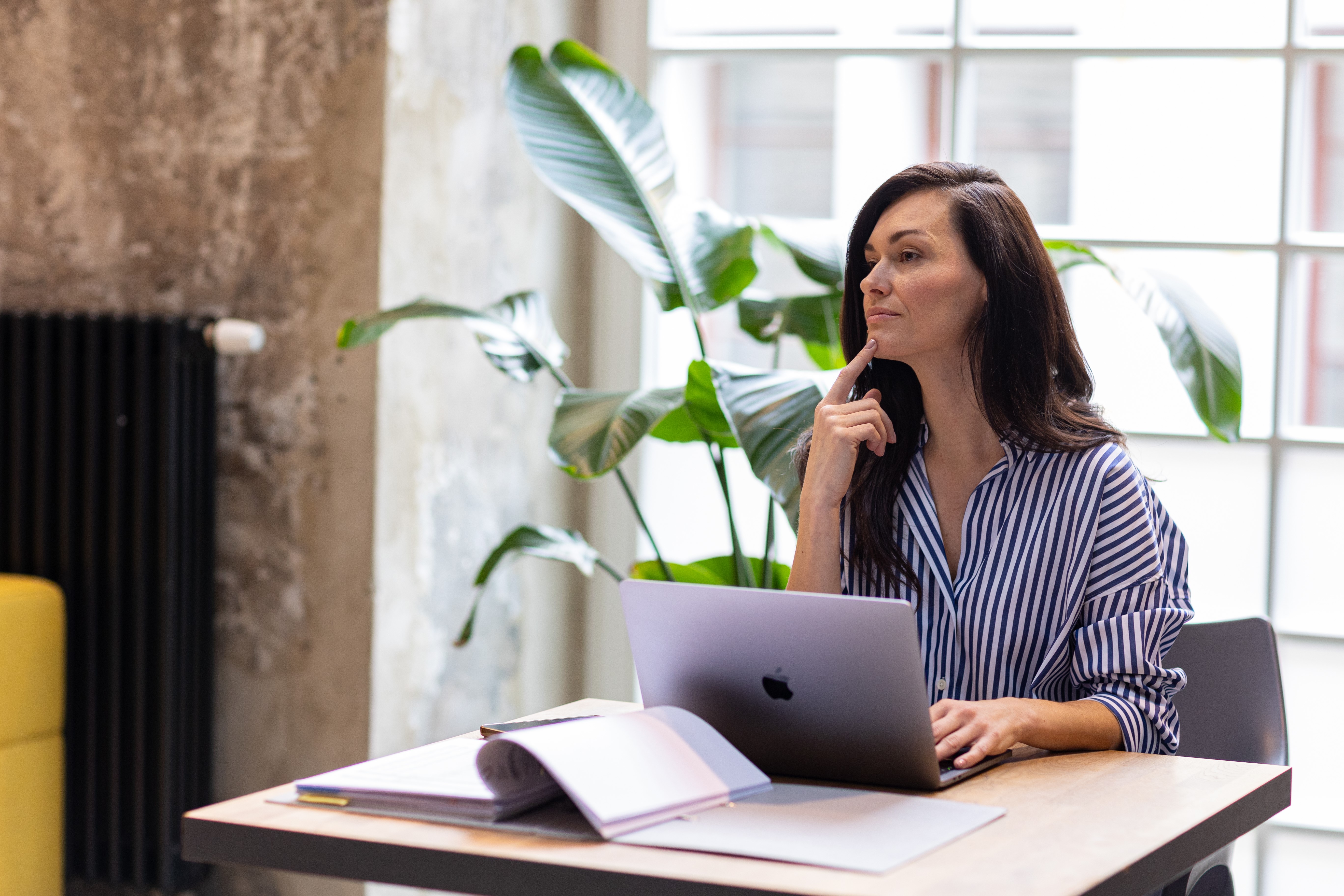 Mõtlik naine töötab sülearvutiga laua taga.