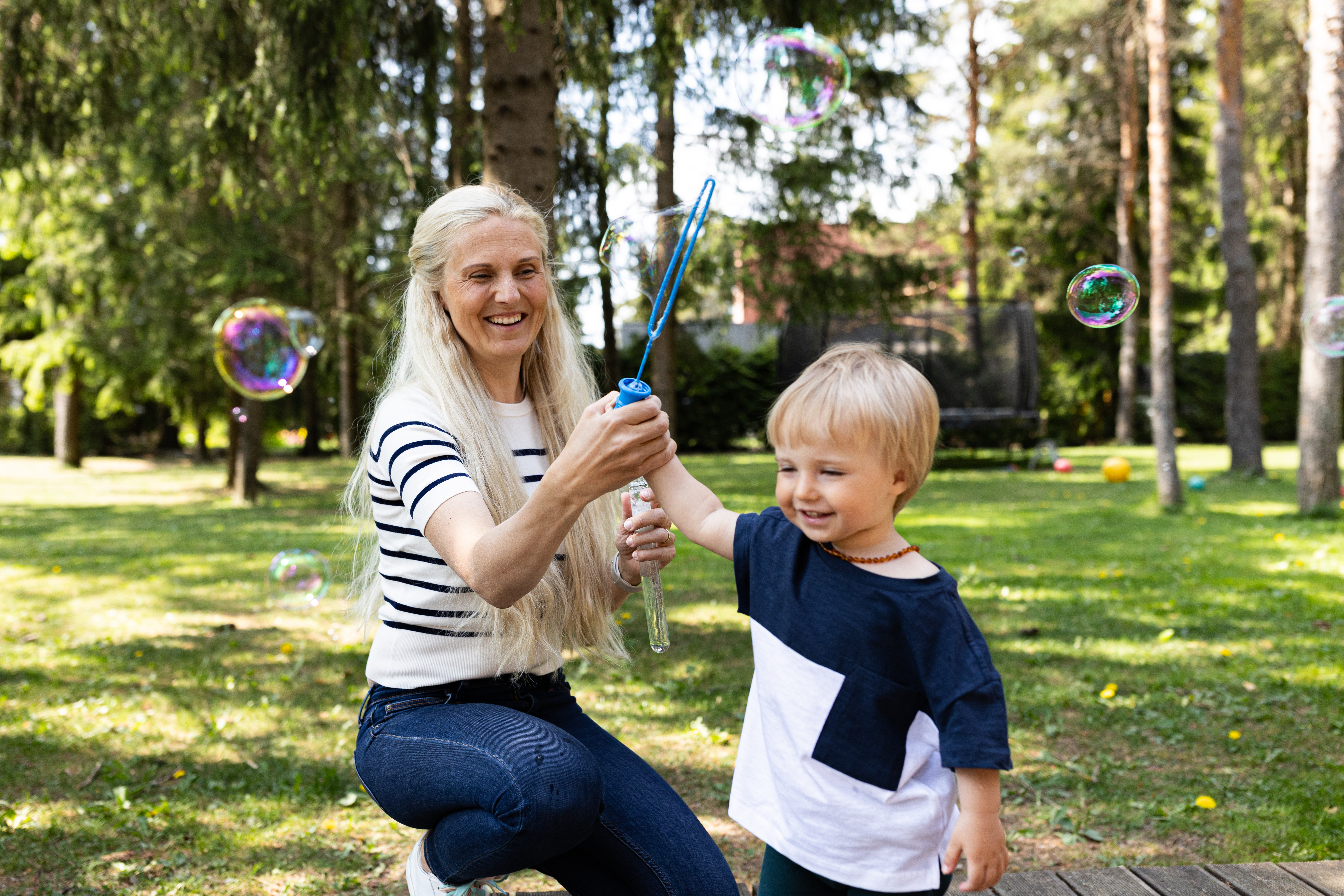Ema ja laps mängivad aias seebimullidega, nende tulevik on tänu järjepidevale kogumisele kindlustatud.