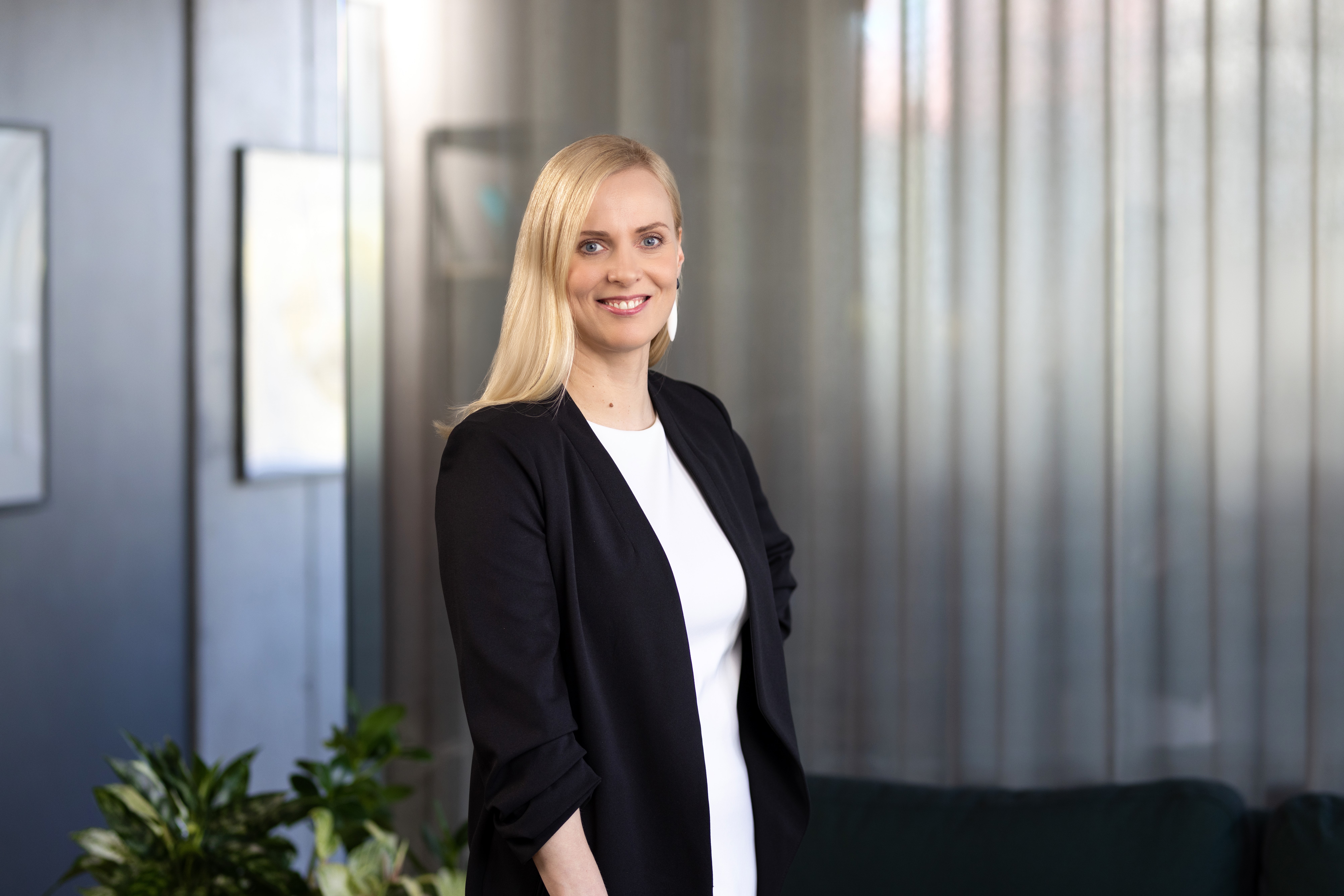 Женщина стоит в офисе и улыбается в камеру.